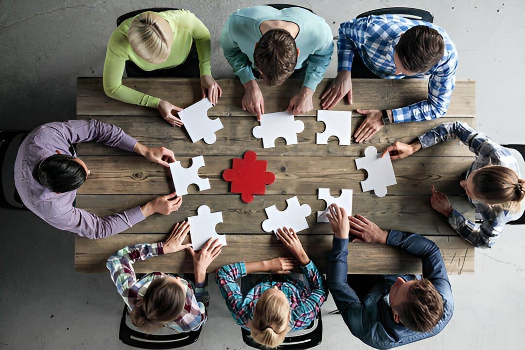 Une équipe autour d’une table, qui assemble les pièces d’un puzzle