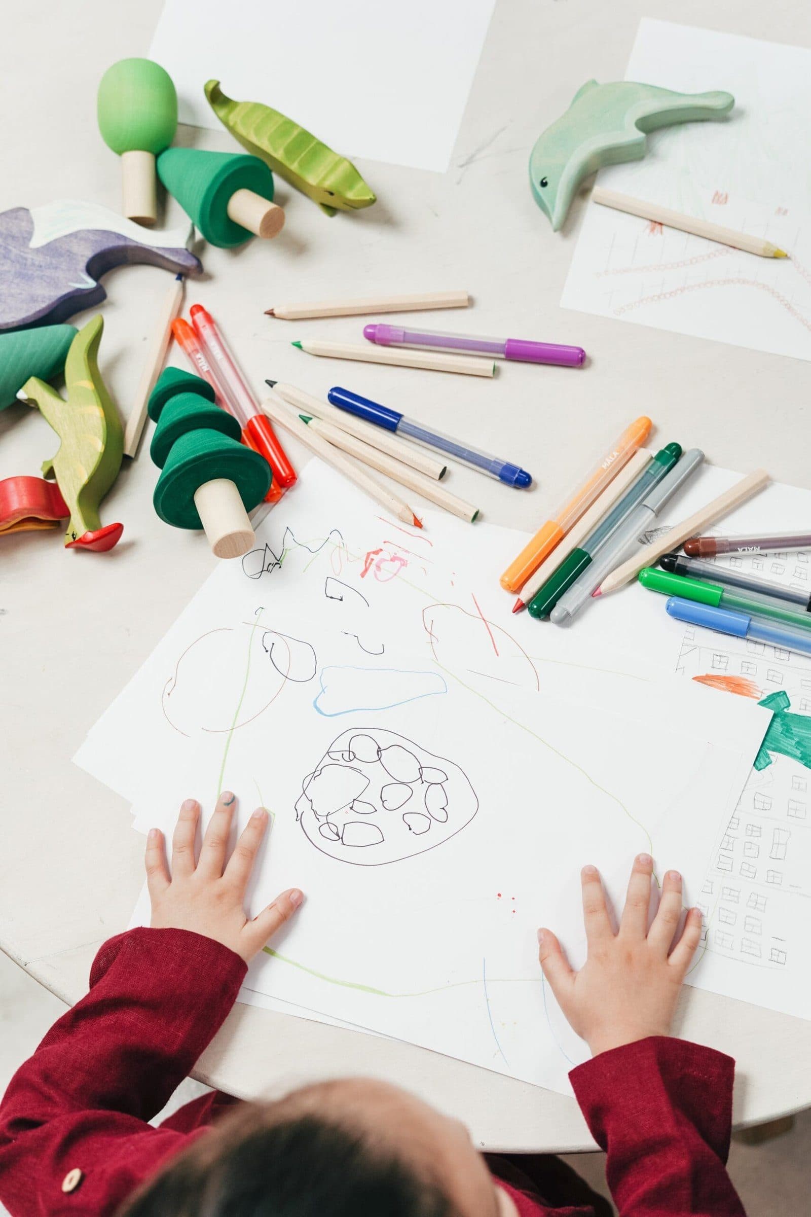 Un enfant dessine, entouré de crayons et de feuilles